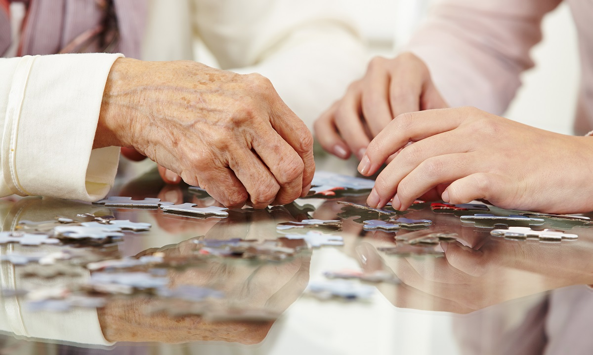 Close-up of an older person's hand and a younger person's hands working on a jigsaw puzzle together.